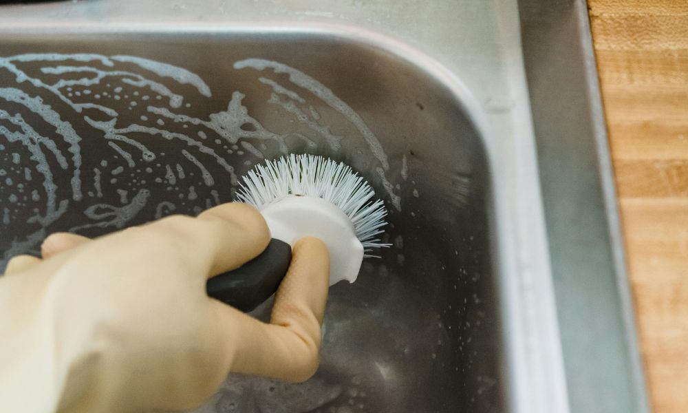 deep cleaning the stainless steel kitchen sink by brushing the the surface with soap and warm water