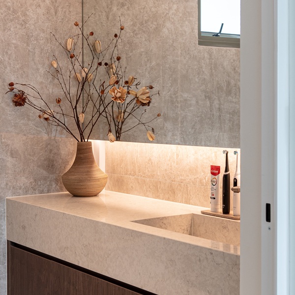 Bathroom vanity featuring an Aurastone countertop with integrated sink and ambient lighting, styled with a wooden vase of dried florals.